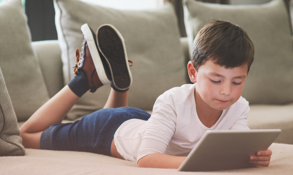Young boy lying on a couch using a tablet—capturing the connection between screen time and emotional health in early childhood.