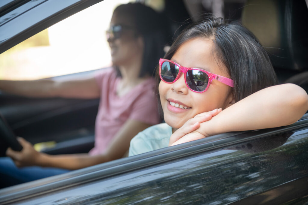 Girl smiling in car with sunglasses—capturing daily mindfulness routines for families on the go.