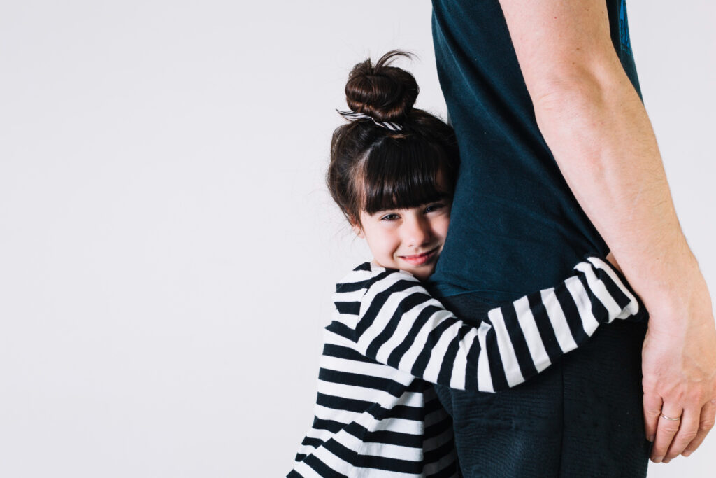 Young girl hugging an adult’s waist while smiling